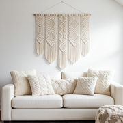 White sofa with textured cushions and a macrame wall hanging in a minimalistic living room.