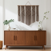 Wooden sideboard with decorative brown macrame wall hanging and plants in a room