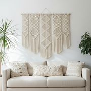 Modern Macrame wall hanging above a beige sofa with decorative pillows in a living room setting.