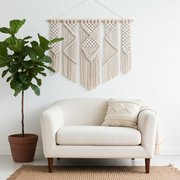 White sofa with a plant and macrame wall hanging in a room.